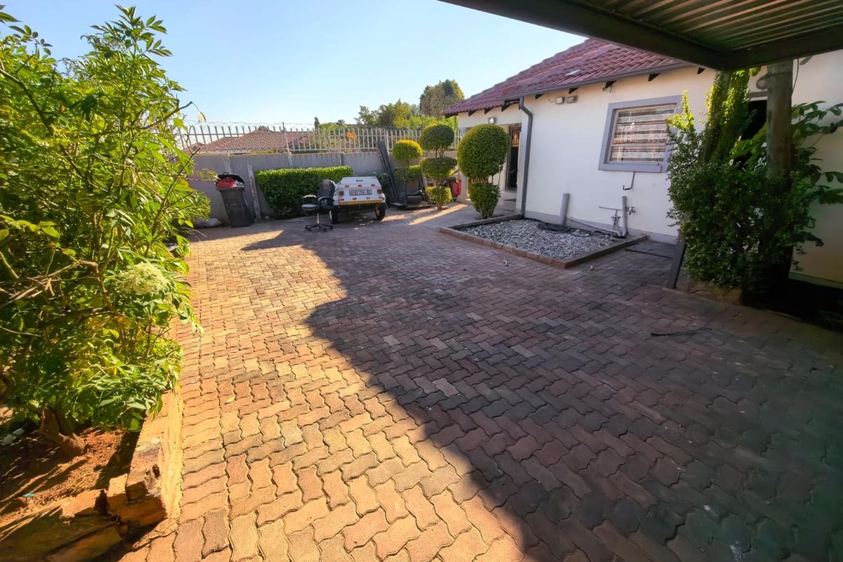 A paved rear courtyard area featuring a covered patio section, security fencing, and established garden borders.