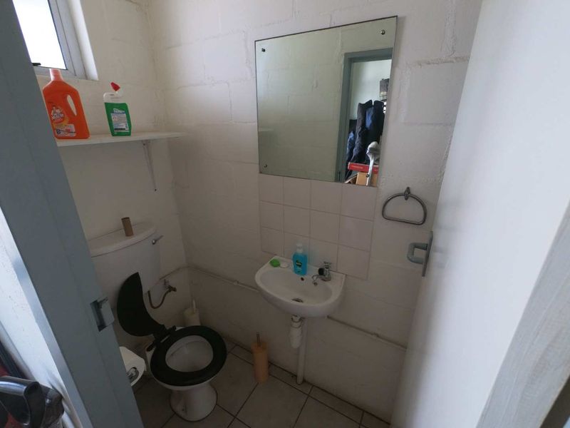 A compact industrial-style bathroom featuring a wall-mounted basin, toilet, and exposed blockwork walls, offering a functional space with potential for cosmetic updates.