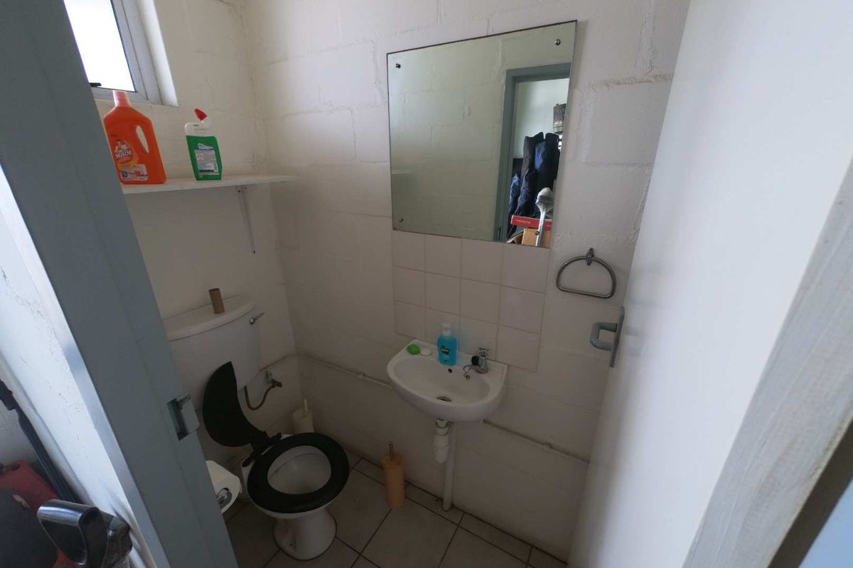 A compact industrial-style bathroom featuring a wall-mounted basin, toilet, and exposed blockwork walls, offering a functional space with potential for cosmetic updates.