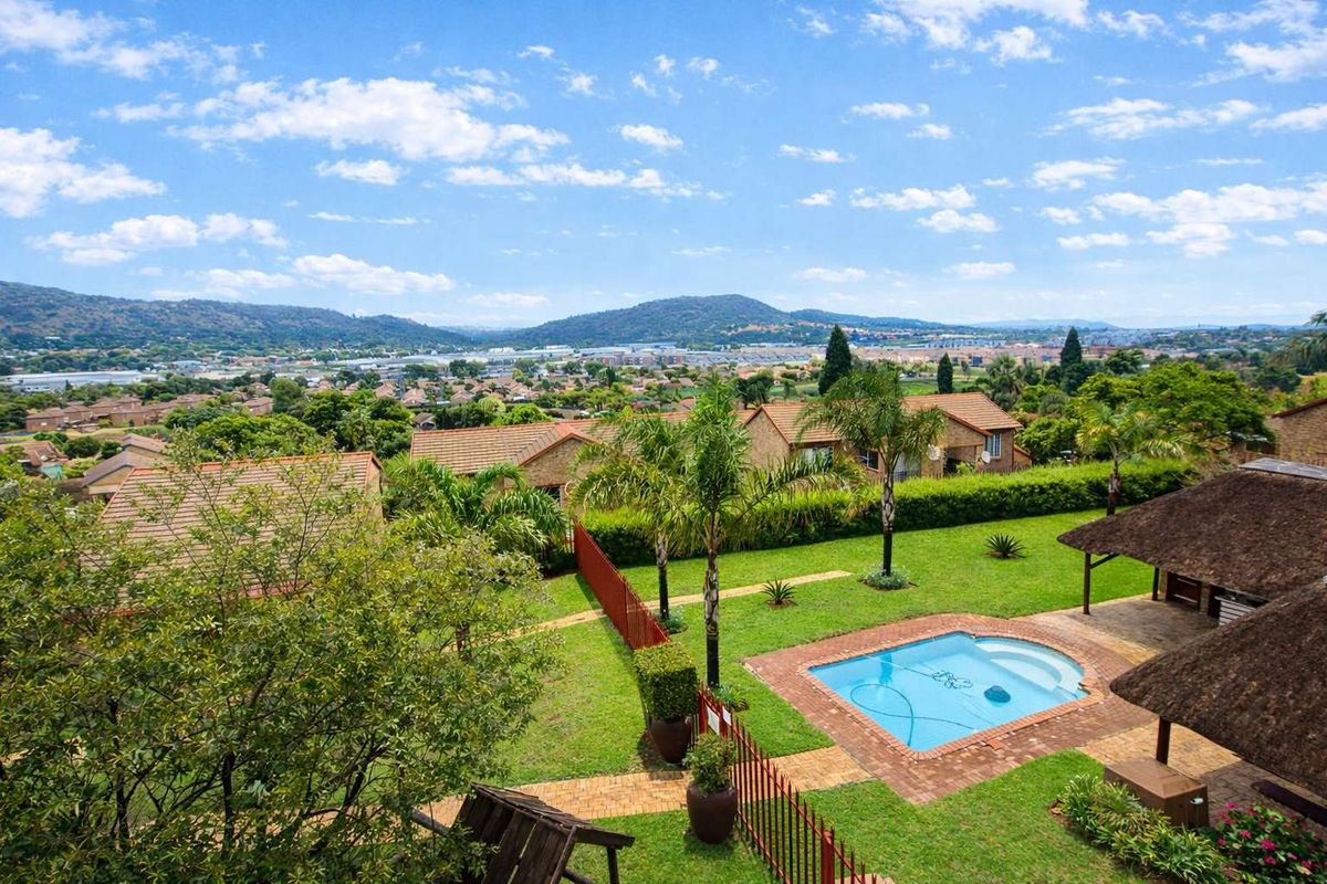 Elevated aerial view of a townhouse complex featuring a private swimming pool, thatched lapa, landscaped garden, and scenic mountain views.