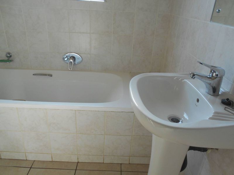 A functional bathroom featuring a standard bathtub, pedestal basin, and neutral ceramic wall and floor tiling.