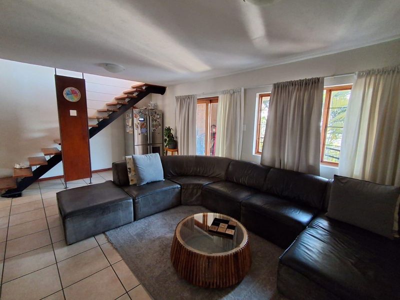Spacious living area featuring tiled flooring, a modern open-tread staircase, and large windows providing natural light with access to an outdoor area.