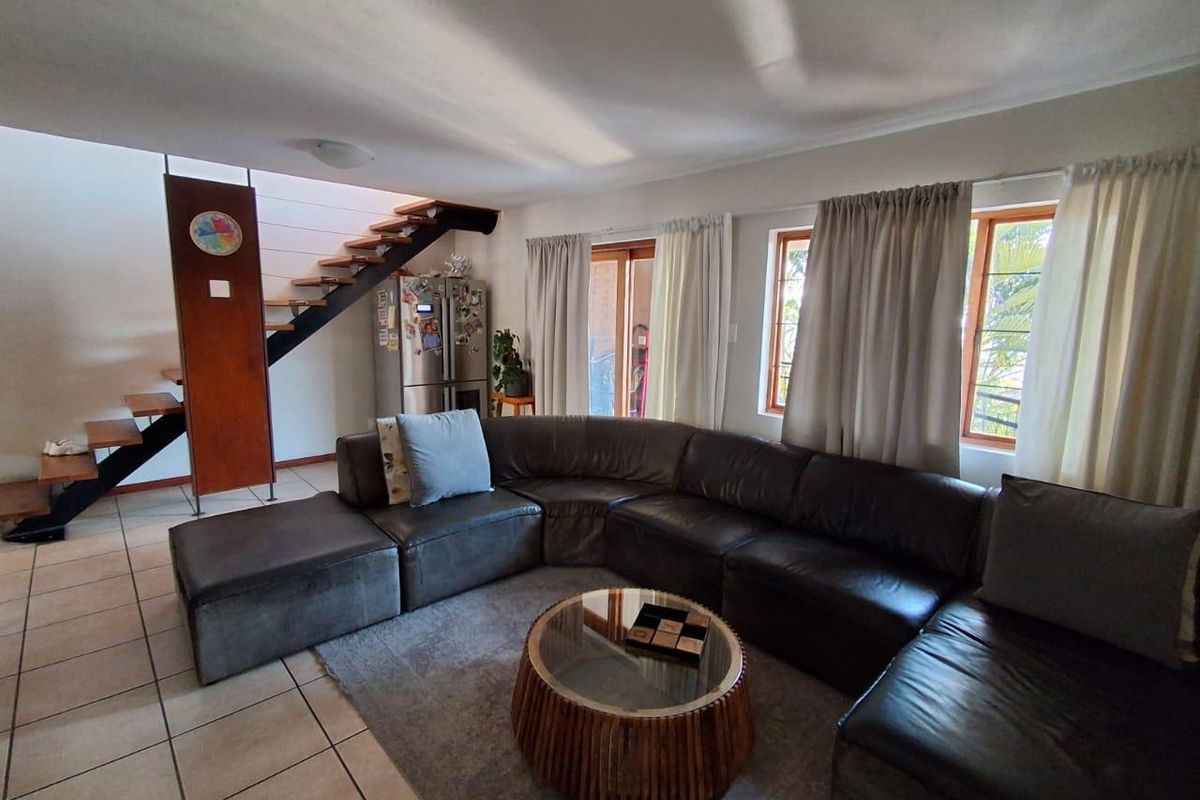 Spacious living area featuring tiled flooring, a modern open-tread staircase, and large windows providing natural light with access to an outdoor area.