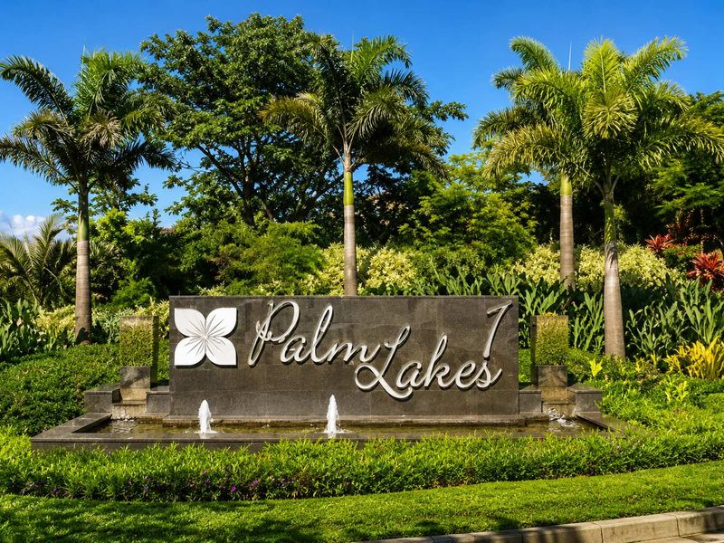 A well-maintained entrance signage for Palm Lakes, featuring a stone monument, integrated water fountains, and lush tropical landscaping.