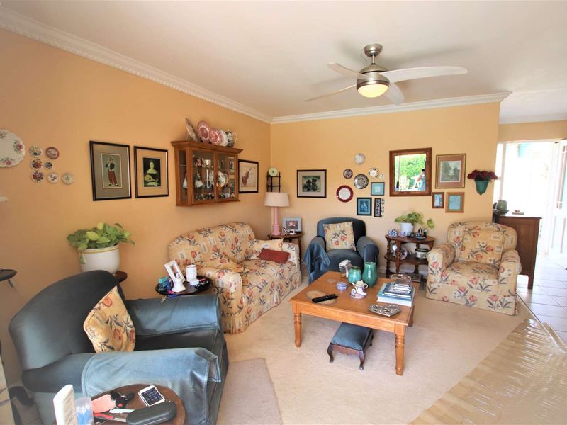 A cozy living room featuring neutral wall tones, crown molding, a ceiling fan, and tiled flooring with access to an adjacent area.