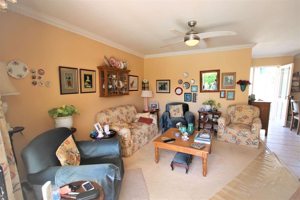 A cozy living room featuring neutral wall tones, crown molding, a ceiling fan, and tiled flooring with access to an adjacent area.