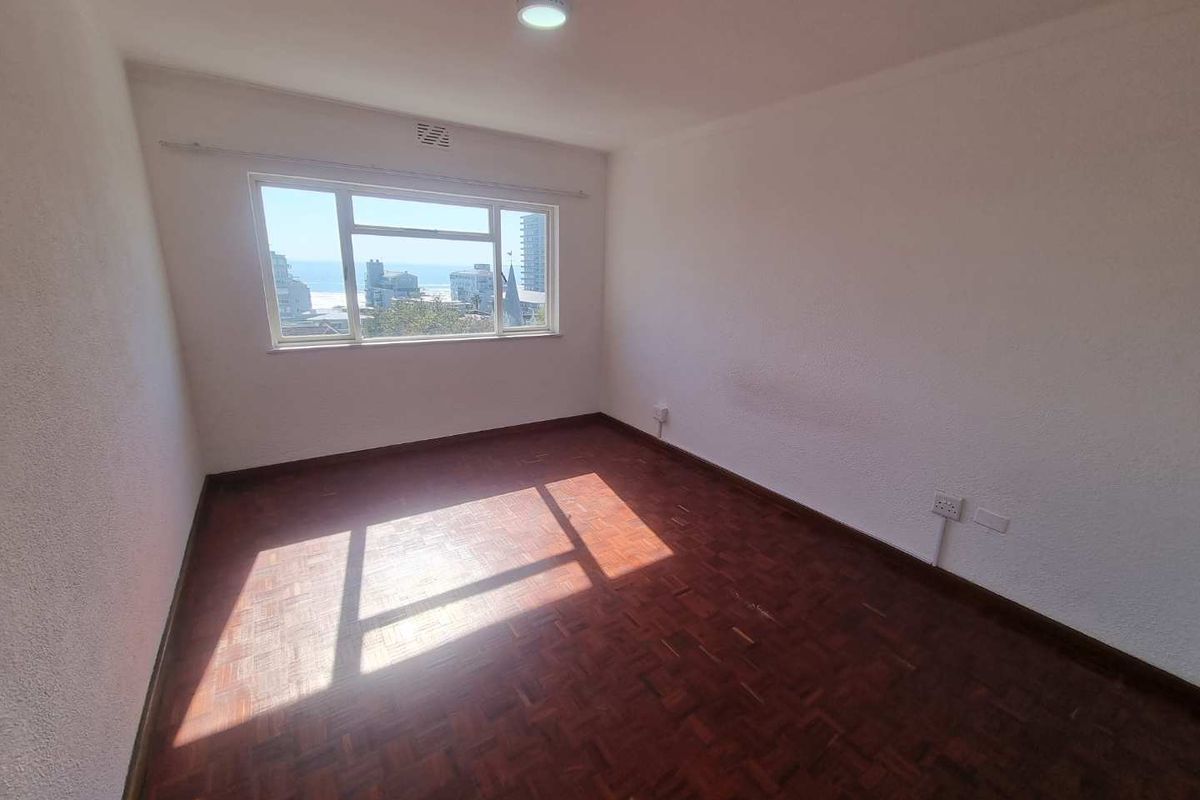 An empty bedroom featuring original parquet flooring, a large window with natural light, and neutral walls, offering a blank canvas for personalization.