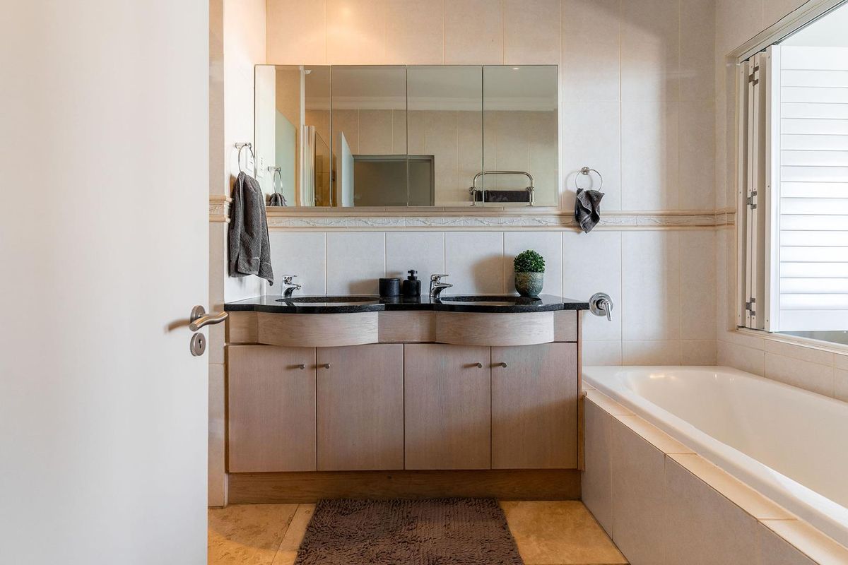 A functional bathroom featuring a double vanity with stone countertop, integrated sinks, large wall-mounted mirror cabinet, and a built-in bathtub.