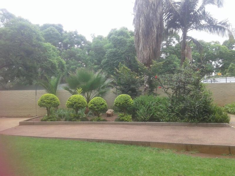 A well-maintained garden area featuring landscaped beds, manicured shrubs, a paved walkway, and a secure perimeter boundary wall.