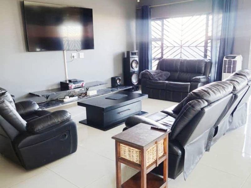 A well-maintained living room featuring neutral tiled flooring, grey accent walls, and a large window with security bars for added safety.