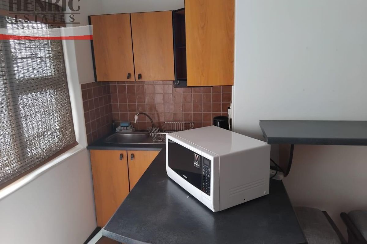 Compact kitchenette featuring wooden cabinetry, dark laminate countertops, a stainless steel sink, and a tiled backsplash.
