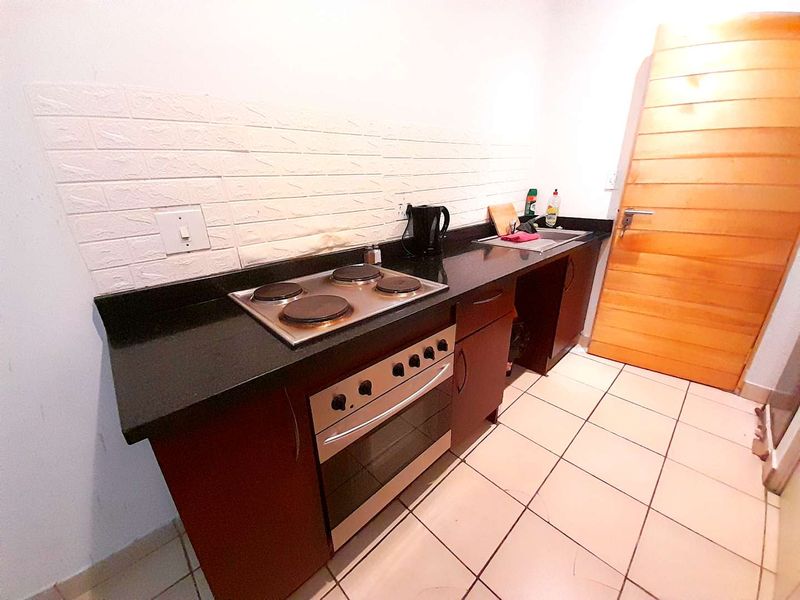 Compact kitchen featuring dark cabinetry, granite countertops, a built-in oven with electric hob, and tiled flooring.