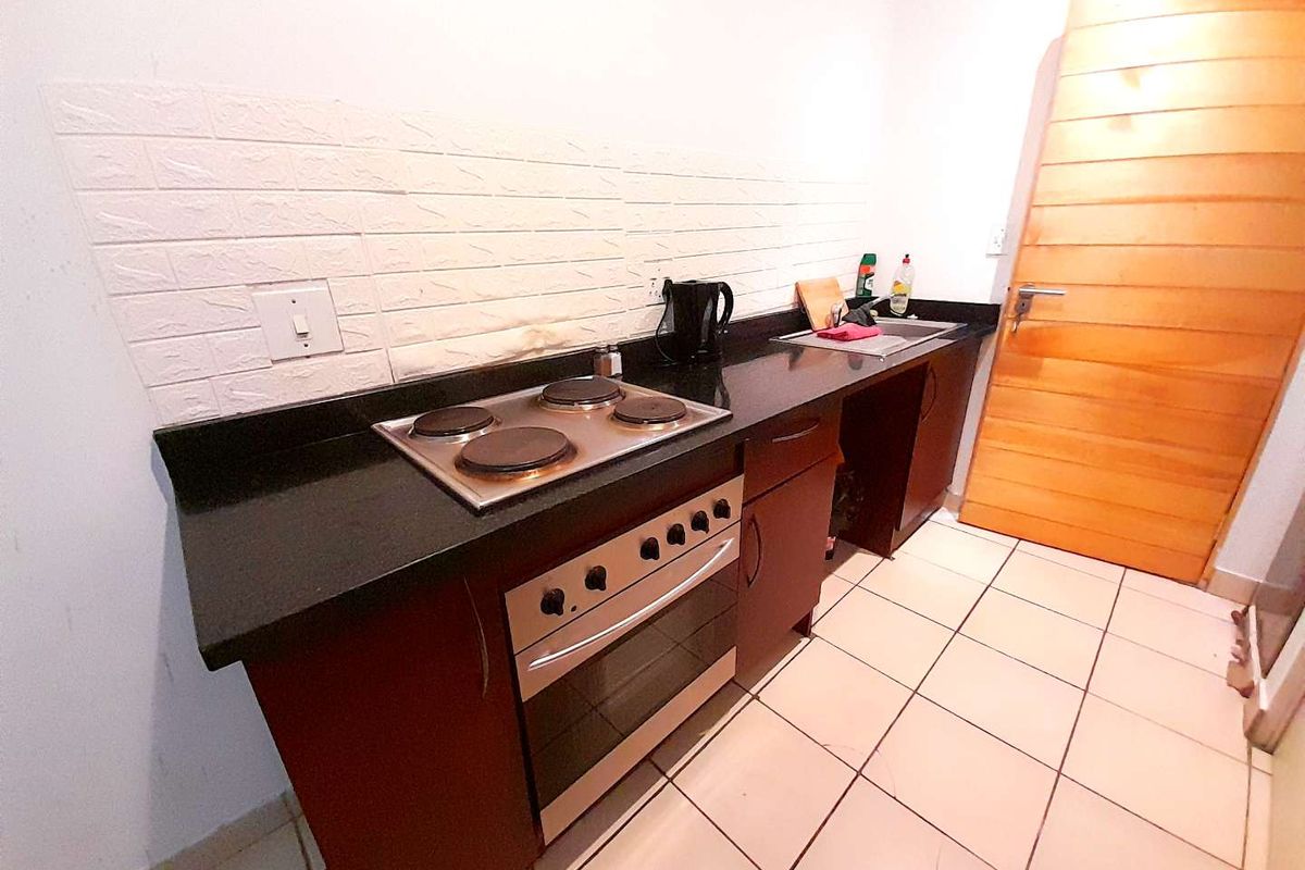 Compact kitchen featuring dark cabinetry, granite countertops, a built-in oven with electric hob, and tiled flooring.