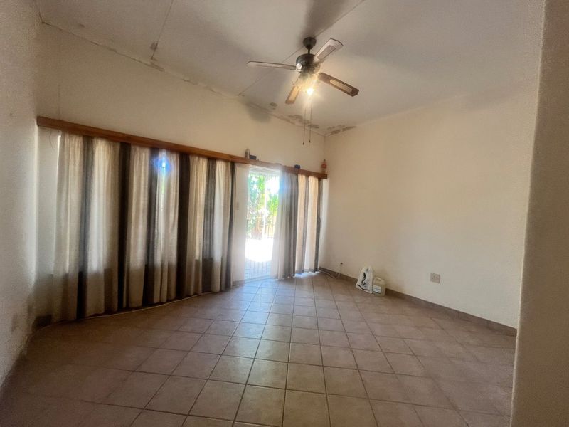 An empty living room featuring tiled flooring, a ceiling fan, and a sliding glass door leading to the exterior, showing signs of ceiling water damage.