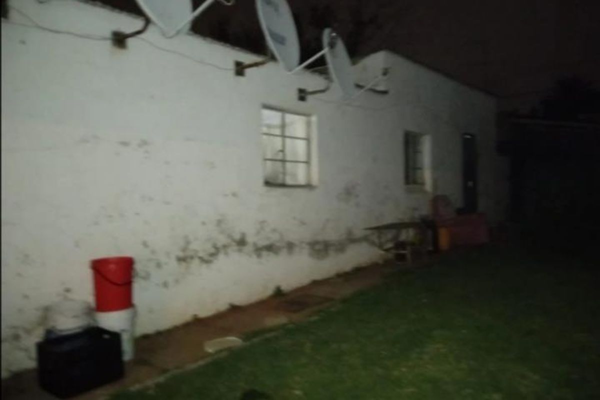 Exterior rear view of the property showing a lawn area and the back facade with multiple satellite dishes mounted on the wall.