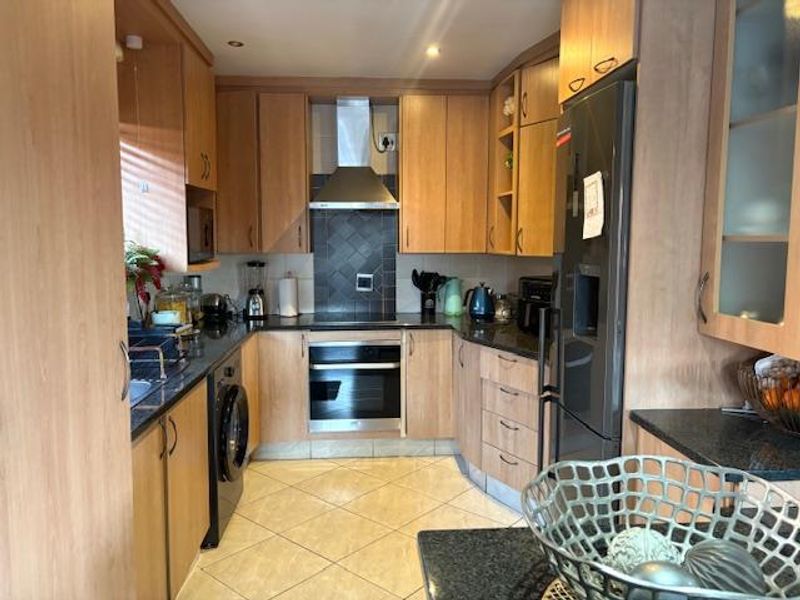 A functional kitchen featuring light wood cabinetry, dark granite countertops, built-in oven, stainless steel extractor fan, and tiled flooring.