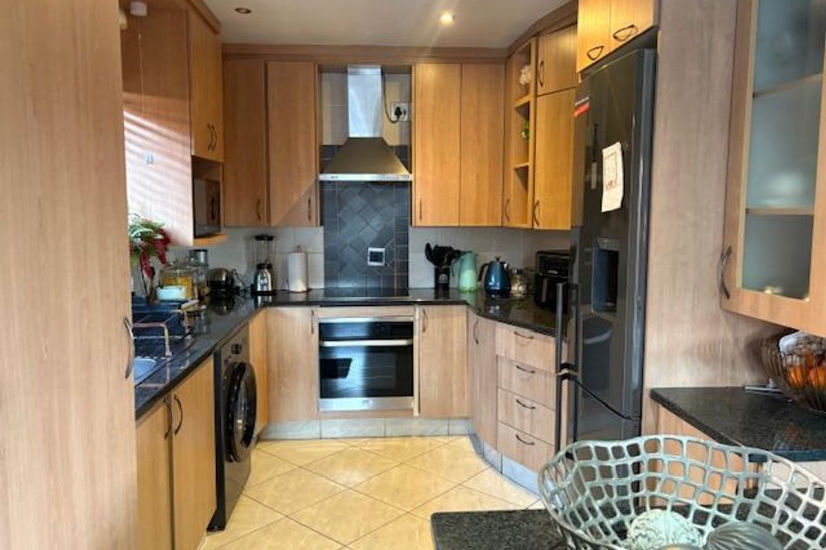 A functional kitchen featuring light wood cabinetry, dark granite countertops, built-in oven, stainless steel extractor fan, and tiled flooring.