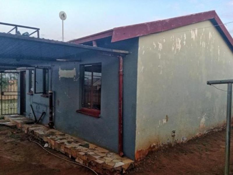 Rear view of the property showing a covered patio area, metal roofing, and exterior walls requiring maintenance and repainting.