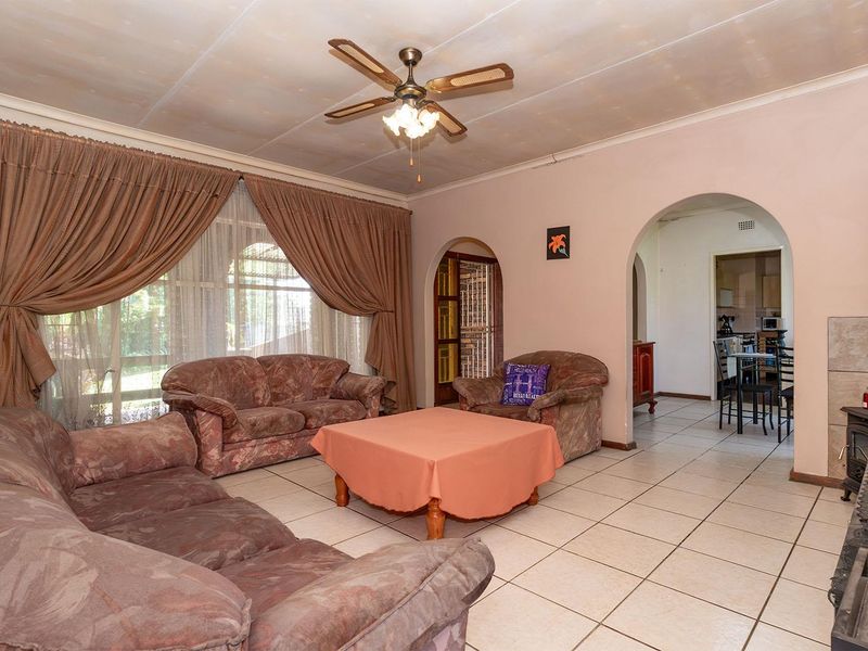 Spacious living room featuring tiled flooring, a ceiling fan, and a freestanding fireplace, with an arched entryway leading to the kitchen area.