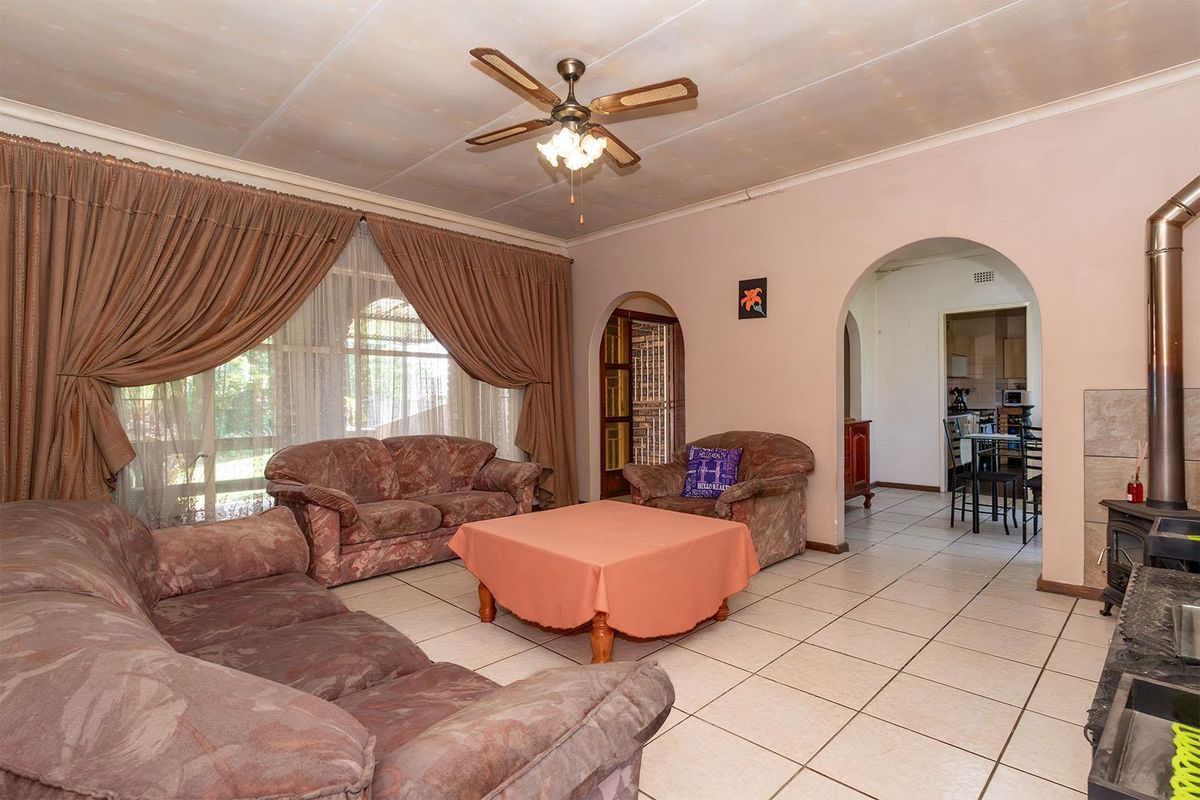 Spacious living room featuring tiled flooring, a ceiling fan, and a freestanding fireplace, with an arched entryway leading to the kitchen area.