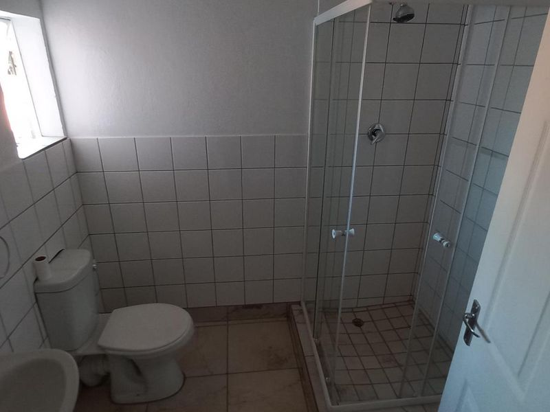 A functional bathroom featuring a glass-enclosed shower, toilet, and washbasin with neutral wall and floor tiling.