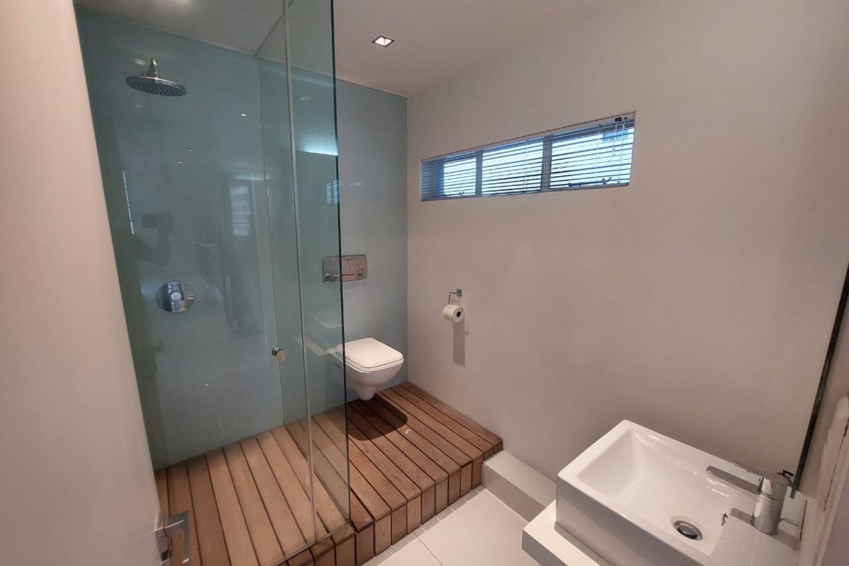 Modern bathroom featuring a wall-mounted toilet, glass-enclosed shower with timber decking, and a sleek wall-mounted vanity basin.