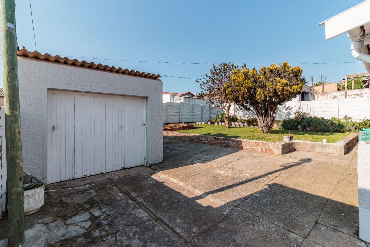 Rear exterior view featuring a detached garage, concrete driveway, and a garden area enclosed by precast concrete boundary walls.
