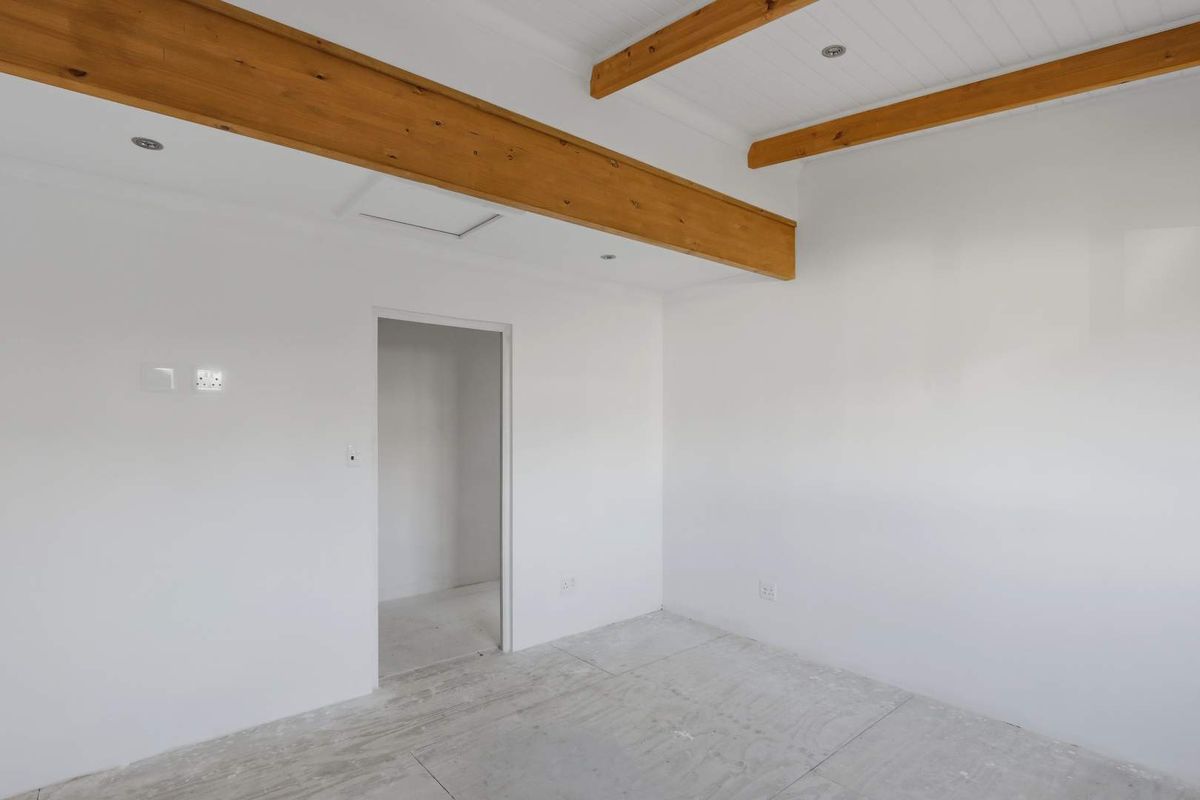 A bright, empty room featuring exposed timber ceiling beams, recessed lighting, and a neutral white finish, ready for final flooring installation.