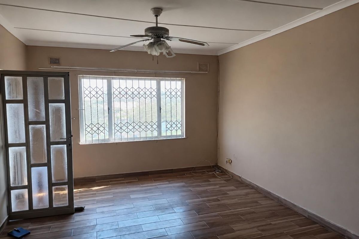An empty living room featuring tiled flooring, a ceiling fan, and security bars on the window.