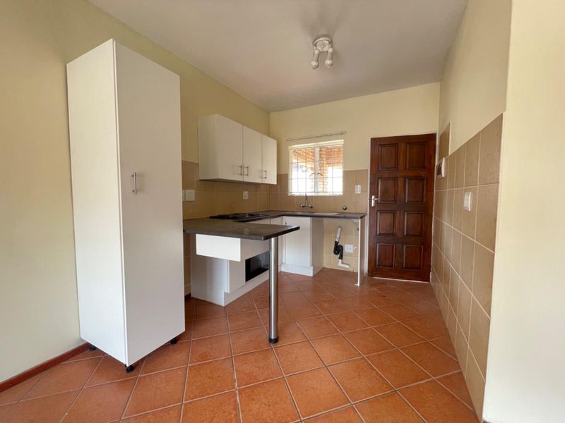 A functional kitchen featuring built-in cabinetry, tiled flooring, and a tiled splashback, offering a clean and practical space for culinary activities.