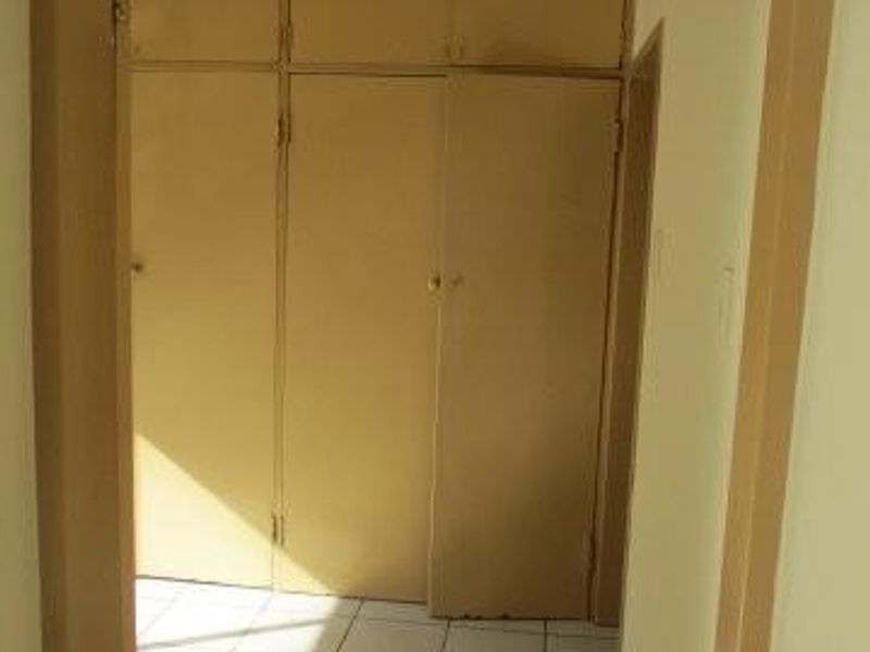An empty bedroom featuring built-in cupboards and tiled flooring, presenting a dated aesthetic in need of modernization.