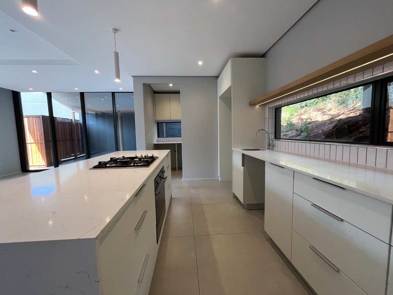 Modern kitchen featuring a large island with gas cooktop, stone countertops, integrated cabinetry, and a separate scullery area with clean, contemporary finishes.