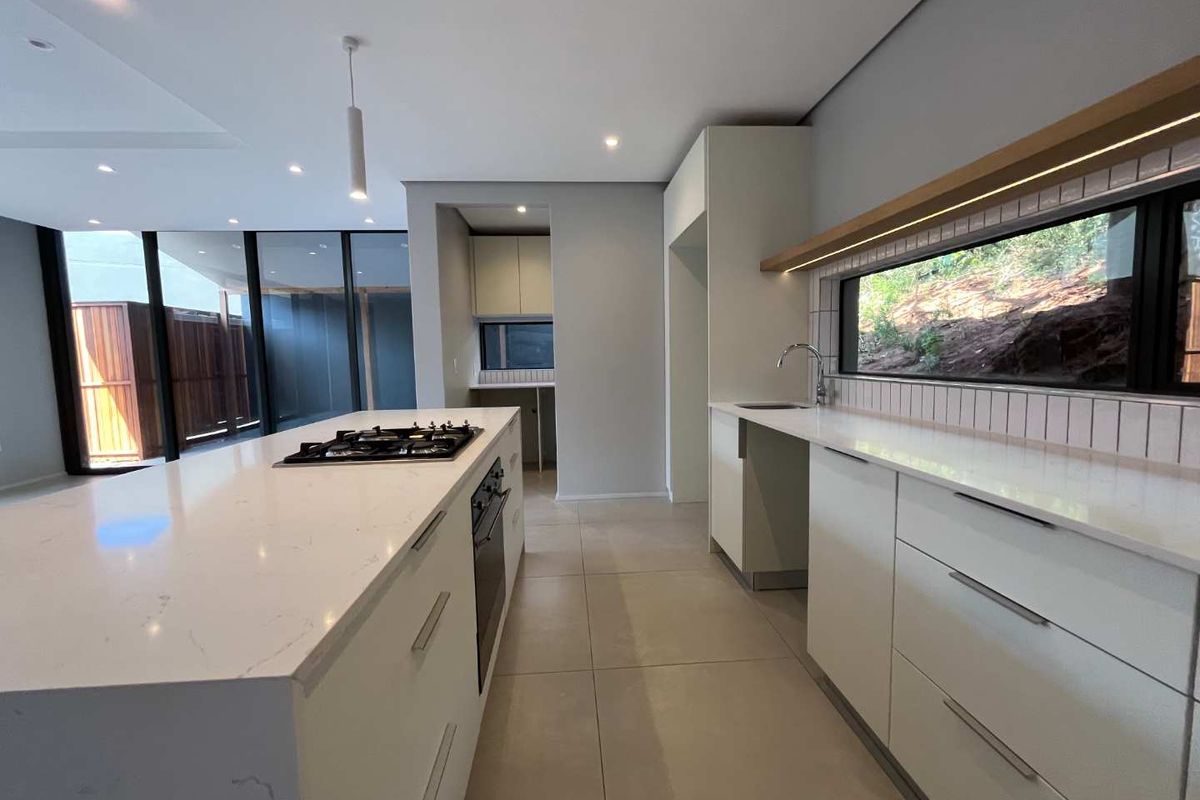 Modern kitchen featuring a large island with gas cooktop, stone countertops, integrated cabinetry, and a separate scullery area with clean, contemporary finishes.