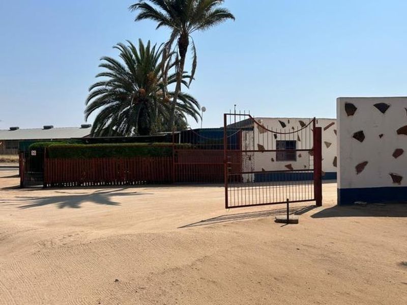 Front exterior view of the industrial property featuring a metal security gate, perimeter fencing, and a large unpaved driveway area.
