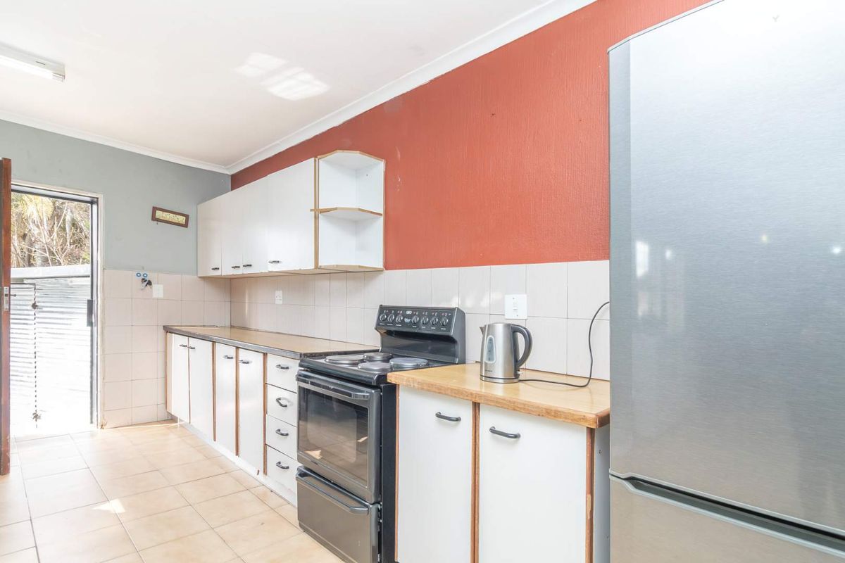A functional kitchen featuring white cabinetry, tiled splashbacks, and a freestanding stove, with direct access to the exterior.