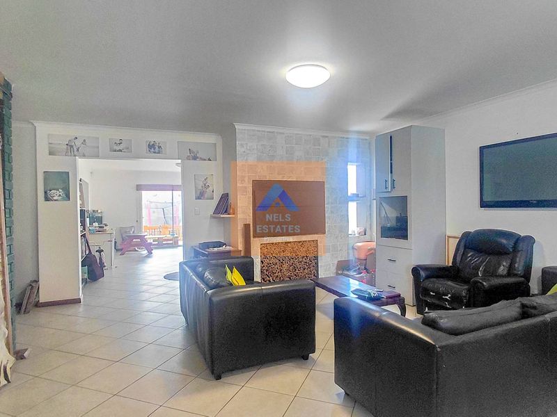 Spacious living room featuring a stone-clad fireplace, built-in cabinetry, and tiled flooring, with an open-plan flow leading to an adjacent area.