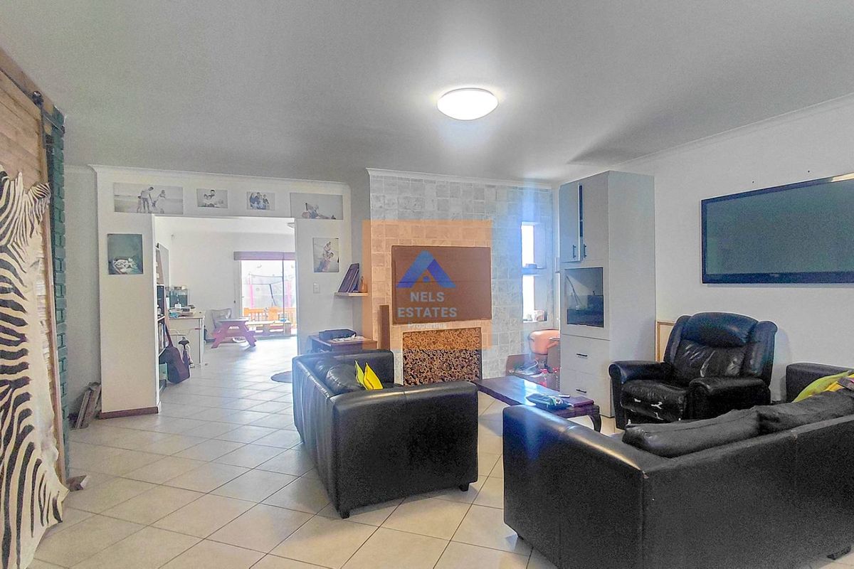 Spacious living room featuring a stone-clad fireplace, built-in cabinetry, and tiled flooring, with an open-plan flow leading to an adjacent area.