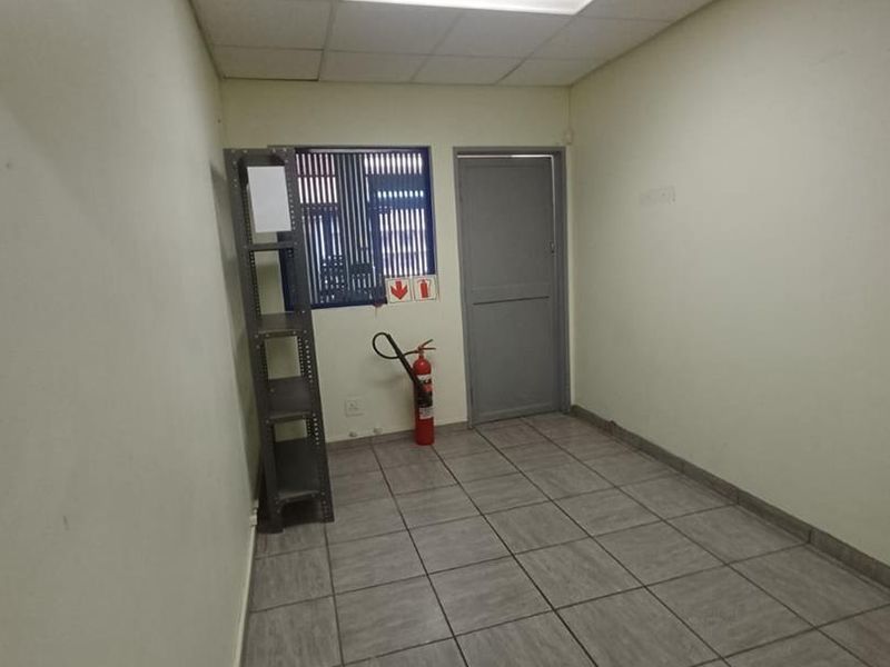 A functional, empty office space featuring tiled flooring, a suspended ceiling with recessed lighting, and security bars on the window.