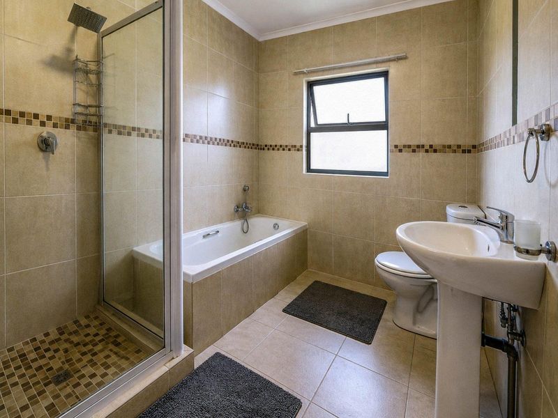 A functional bathroom featuring a separate shower enclosure, bathtub, pedestal basin, and toilet with neutral wall and floor tiling.