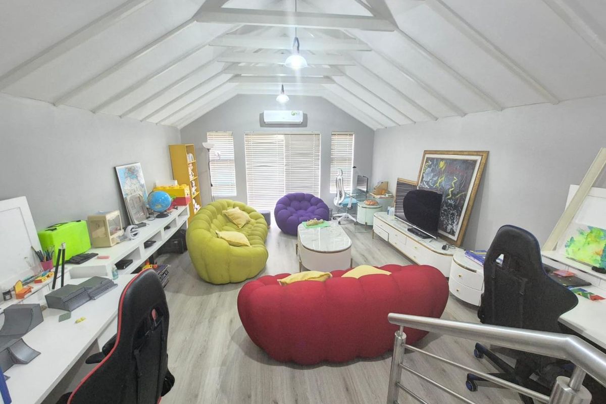 Spacious attic-style living room featuring vaulted ceilings with exposed beams, light wood-look flooring, and a wall-mounted air conditioning unit.