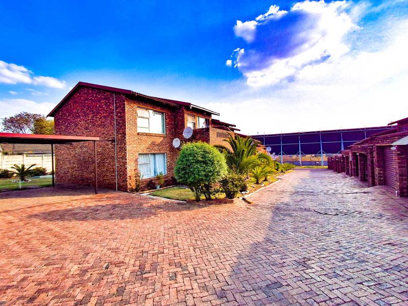 A view of the facebrick cluster unit exterior featuring a paved driveway, carport, and established garden area.