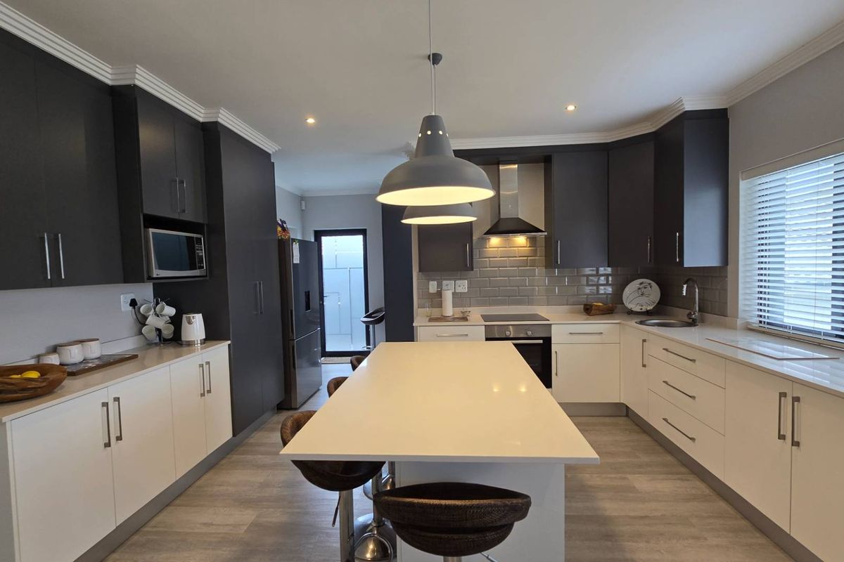 Modern kitchen featuring two-tone cabinetry, stone countertops, a central island, built-in oven, hob, extractor fan, and subway tile backsplash.