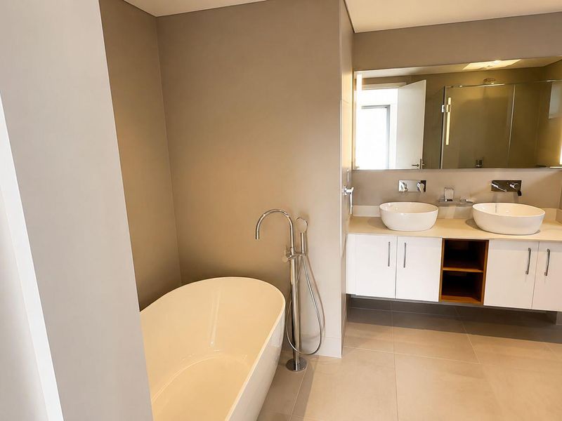 Modern bathroom featuring a sleek freestanding bathtub, double vessel sink vanity with wall-mounted fixtures, and a large backlit mirror.