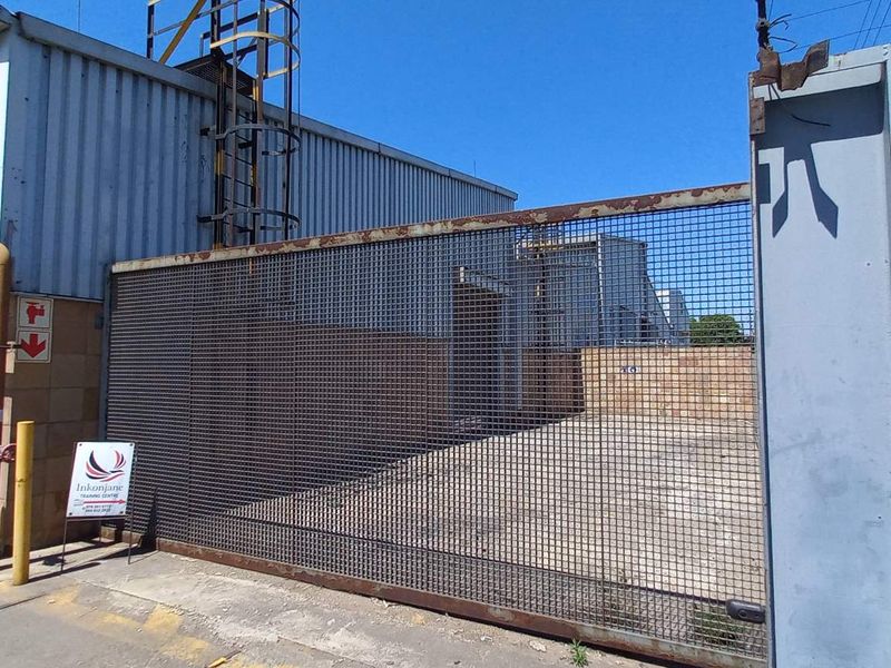 Industrial property exterior featuring a large metal sliding security gate, corrugated metal cladding, and a paved driveway area.