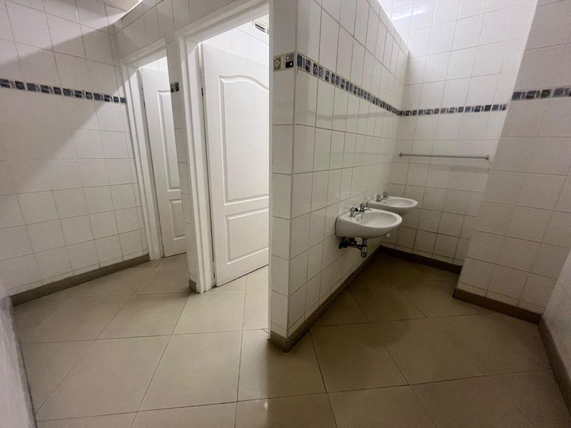 A functional communal bathroom area featuring tiled walls and floors with two wall-mounted washbasins and multiple access doors.