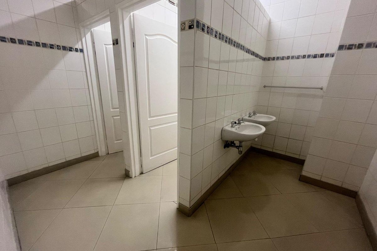 A functional communal bathroom area featuring tiled walls and floors with two wall-mounted washbasins and multiple access doors.