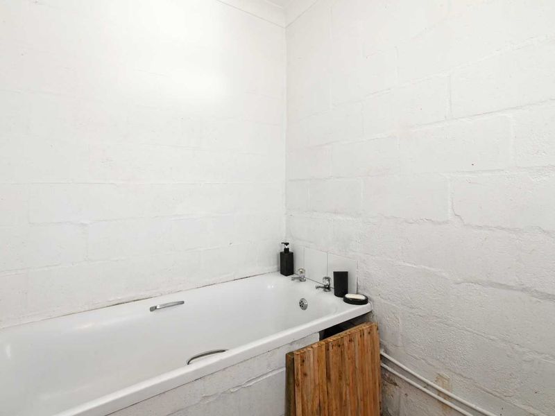 A basic bathroom featuring a standard bathtub with exposed plumbing and unfinished painted blockwork walls.