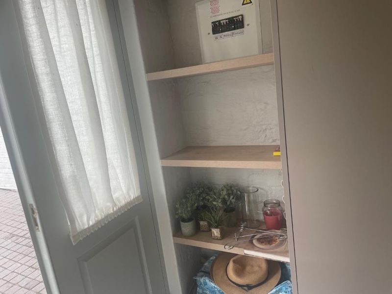 A utility nook featuring built-in shelving and an accessible electrical distribution board, located adjacent to an external door.