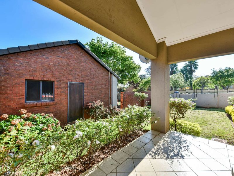 A covered patio area overlooking a private garden with brick exterior walls and tiled flooring.