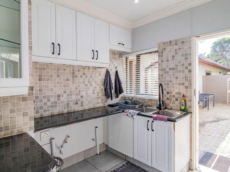 A functional scullery featuring granite countertops, tiled splashbacks, built-in cabinetry, and direct access to the rear outdoor area.